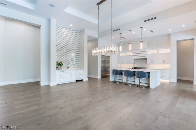 kitchen featuring high end fridge, white cabinetry, a kitchen island with sink, a kitchen breakfast bar, and a chandelier