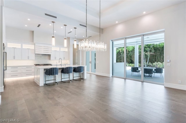 kitchen with an island with sink, light hardwood / wood-style floors, decorative light fixtures, a breakfast bar area, and white cabinetry