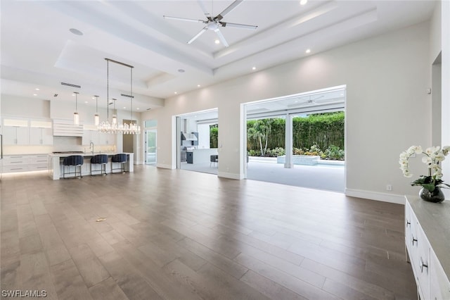 unfurnished living room featuring ceiling fan with notable chandelier, a towering ceiling, a raised ceiling, dark hardwood / wood-style floors, and sink