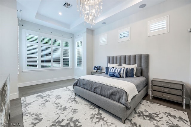 bedroom with an inviting chandelier, a tray ceiling, and wood-type flooring