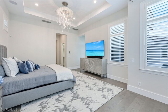 bedroom featuring a raised ceiling, multiple windows, light wood-type flooring, and an inviting chandelier