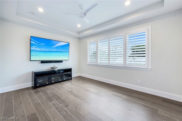 unfurnished living room with a raised ceiling, ceiling fan, and hardwood / wood-style flooring