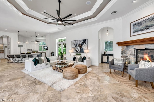 tiled living room featuring a healthy amount of sunlight, a tray ceiling, ceiling fan, and a fireplace