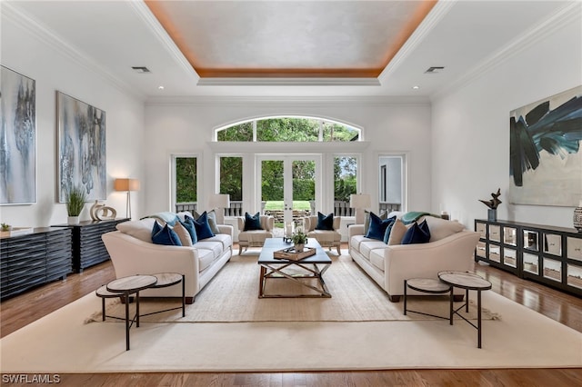 living room featuring a towering ceiling, ornamental molding, a tray ceiling, and light wood-type flooring