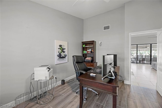 home office with visible vents, baseboards, a high ceiling, and wood tiled floor