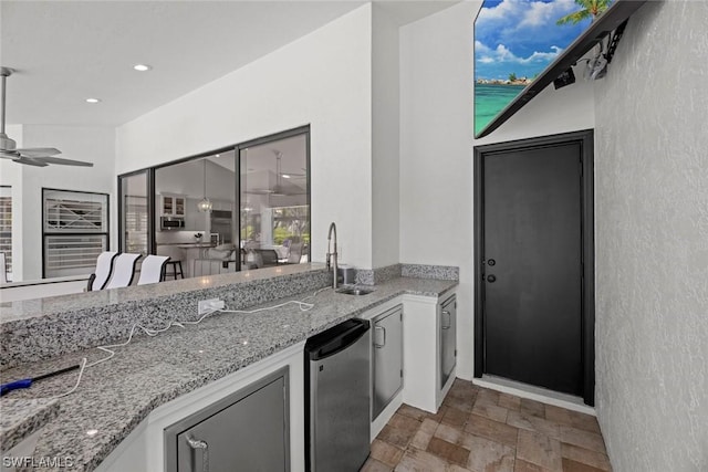 kitchen featuring stone finish floor, a sink, light stone counters, fridge, and ceiling fan