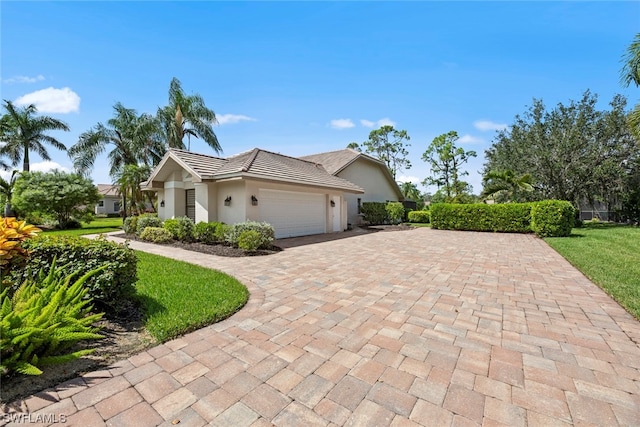 view of side of property featuring decorative driveway, a tiled roof, an attached garage, and stucco siding