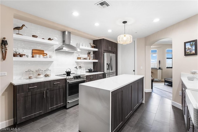 kitchen featuring appliances with stainless steel finishes, hanging light fixtures, a center island, dark brown cabinetry, and wall chimney exhaust hood