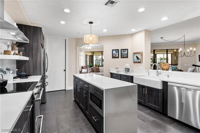 kitchen with wall chimney exhaust hood, sink, hanging light fixtures, appliances with stainless steel finishes, and a kitchen island