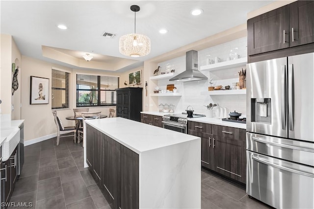 kitchen featuring appliances with stainless steel finishes, a tray ceiling, a kitchen island, pendant lighting, and range hood