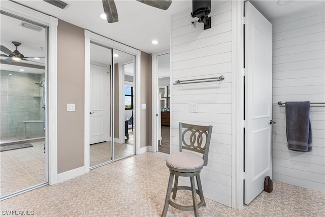 bathroom featuring ceiling fan, tile patterned floors, wood walls, and a tile shower