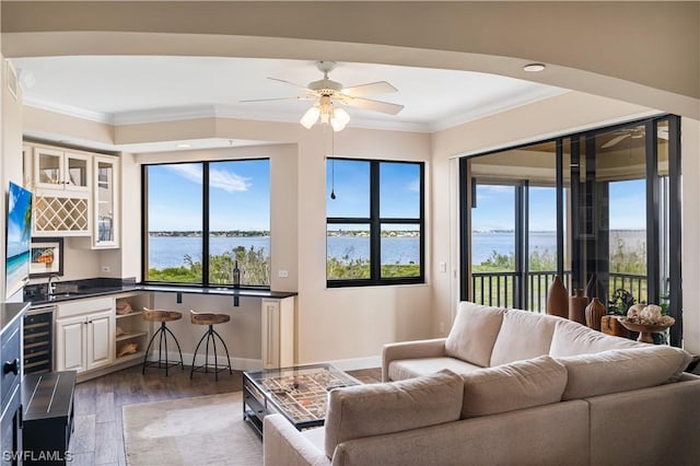 living room featuring dark wood-type flooring, ornamental molding, indoor wet bar, and a water view