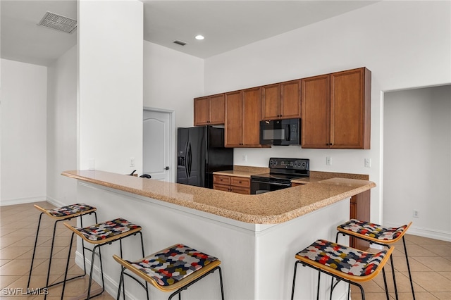 kitchen featuring black appliances, kitchen peninsula, light tile patterned floors, and a breakfast bar