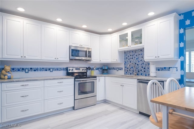 kitchen featuring sink, appliances with stainless steel finishes, white cabinetry, light stone counters, and light hardwood / wood-style floors