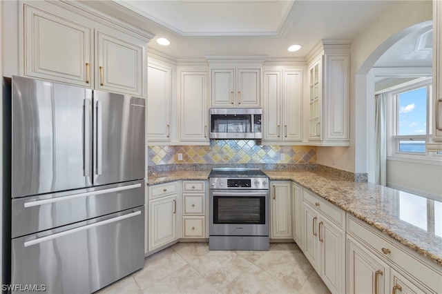 kitchen featuring light tile floors, ornamental molding, appliances with stainless steel finishes, light stone countertops, and tasteful backsplash