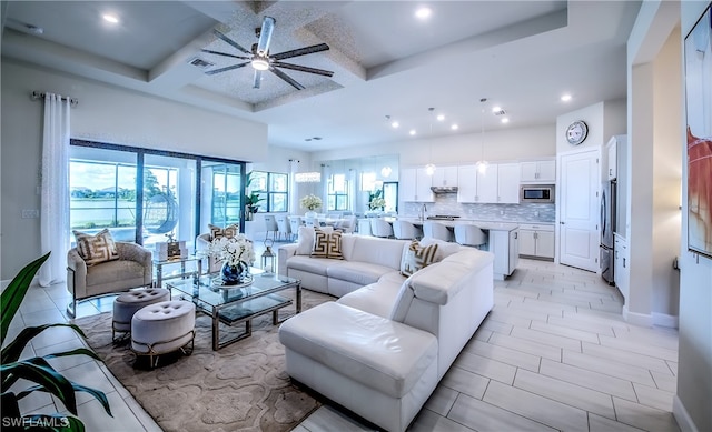 living room featuring coffered ceiling, light tile flooring, a raised ceiling, and ceiling fan