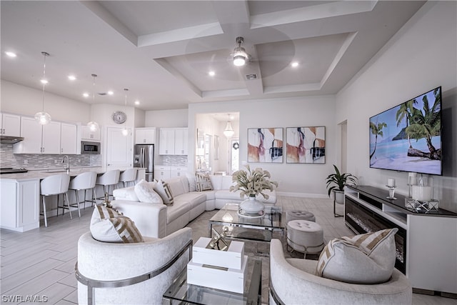 living room featuring light tile floors, coffered ceiling, ceiling fan, and a raised ceiling