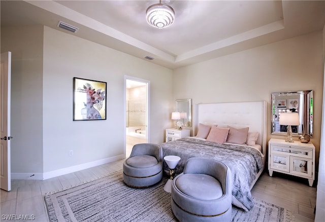 bedroom featuring a raised ceiling, light hardwood / wood-style floors, and ensuite bathroom