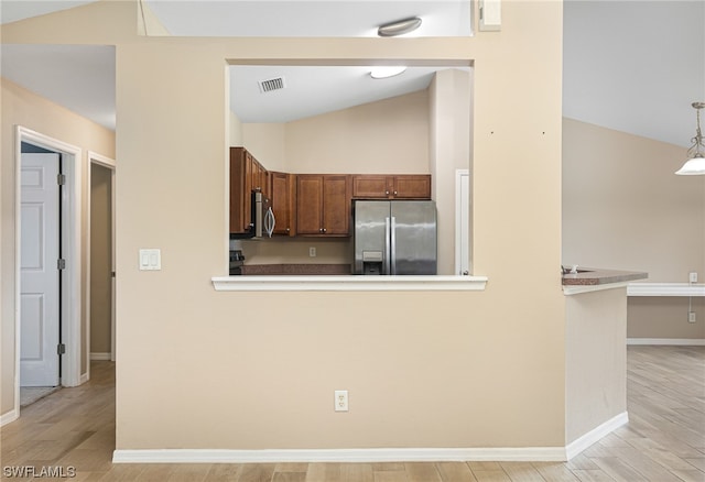 kitchen featuring pendant lighting, vaulted ceiling, light wood-type flooring, appliances with stainless steel finishes, and kitchen peninsula