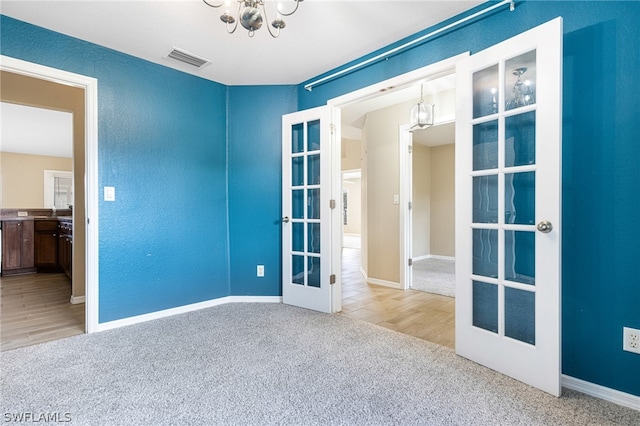 unfurnished room with carpet flooring, french doors, and an inviting chandelier