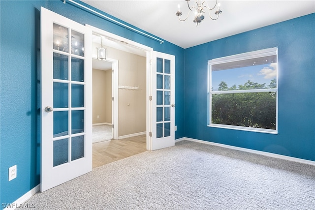 carpeted empty room with a chandelier and french doors