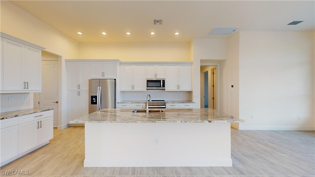 kitchen with white cabinets, light stone countertops, stainless steel appliances, and an island with sink