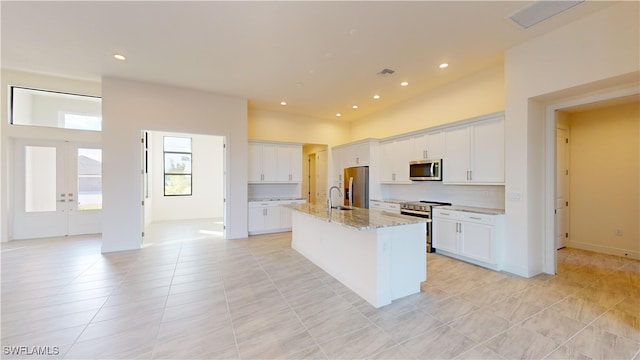 kitchen featuring stainless steel appliances, white cabinetry, a center island with sink, and light stone counters