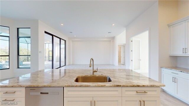 kitchen with light stone countertops, white cabinets, stainless steel dishwasher, and sink