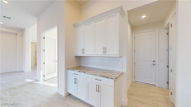 kitchen featuring tasteful backsplash, white cabinetry, light tile patterned floors, and light stone counters