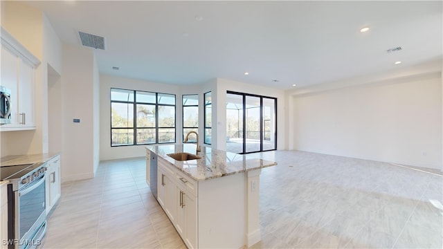 kitchen featuring sink, light stone counters, a kitchen island with sink, white cabinets, and appliances with stainless steel finishes