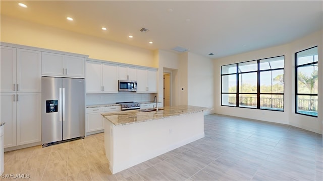 kitchen featuring a kitchen island with sink, white cabinets, light stone countertops, and appliances with stainless steel finishes