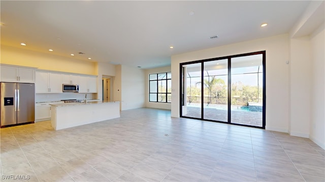 kitchen with light stone countertops, white cabinetry, stainless steel appliances, an island with sink, and light tile patterned floors