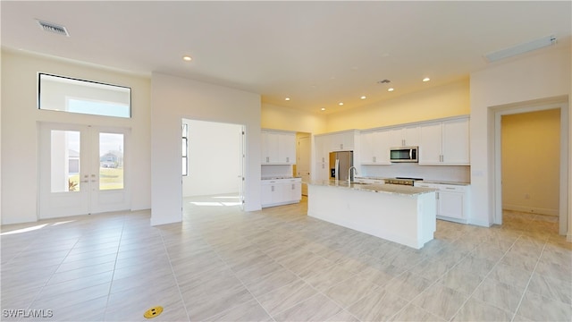 kitchen with french doors, white cabinets, an island with sink, light stone counters, and stainless steel appliances