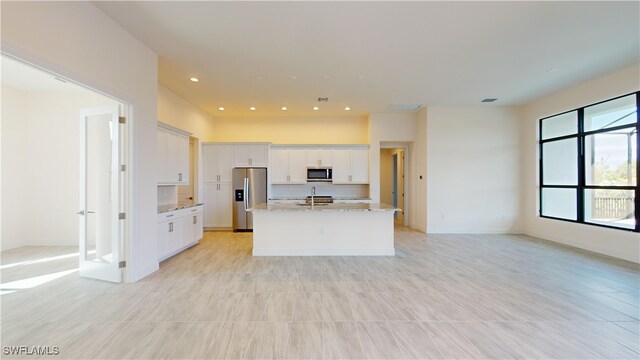 kitchen with light stone counters, stainless steel appliances, a kitchen island with sink, sink, and white cabinets