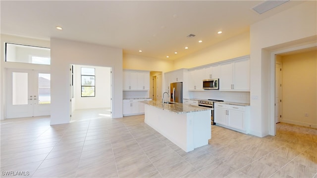 kitchen featuring light stone counters, stainless steel appliances, white cabinets, an island with sink, and light tile patterned flooring