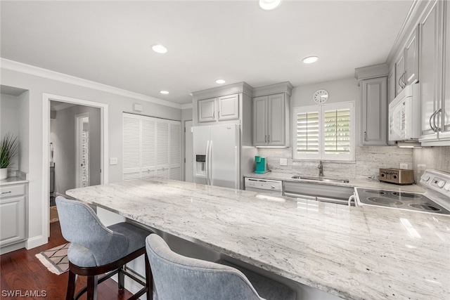 kitchen with a breakfast bar, white appliances, light stone countertops, and sink