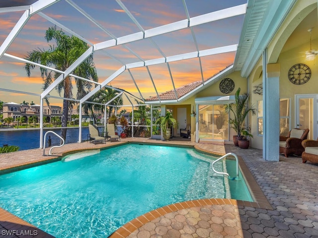 pool at dusk with glass enclosure and a patio area