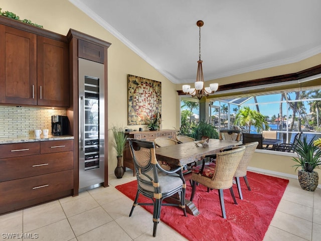 dining area with an inviting chandelier, lofted ceiling, crown molding, and light tile flooring
