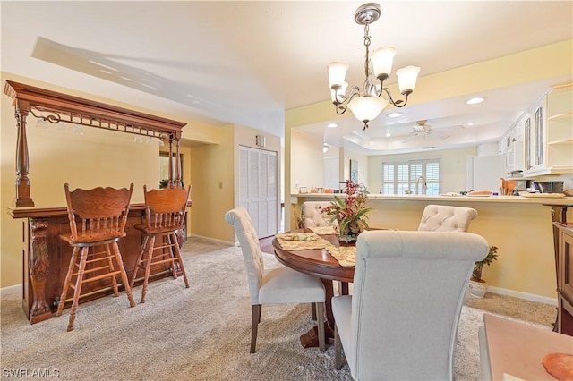 carpeted dining space featuring ceiling fan with notable chandelier, a raised ceiling, and sink