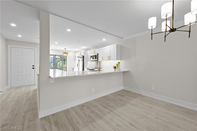 kitchen with a chandelier, stainless steel appliances, kitchen peninsula, light hardwood / wood-style flooring, and white cabinetry