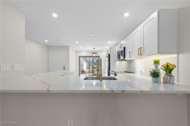 kitchen with kitchen peninsula, stainless steel appliances, white cabinetry, and light stone counters