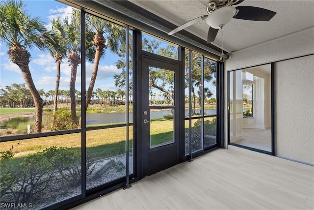 unfurnished sunroom with ceiling fan and a water view