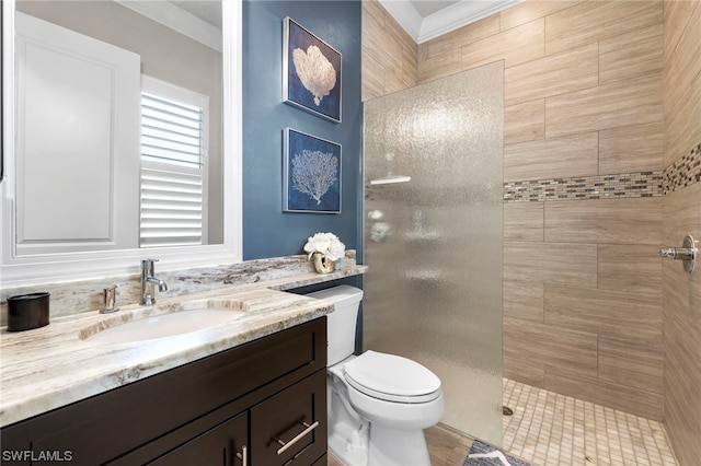 bathroom with toilet, tiled shower, ornamental molding, and vanity