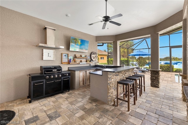 kitchen with a center island, wall chimney exhaust hood, sink, ceiling fan, and a breakfast bar area