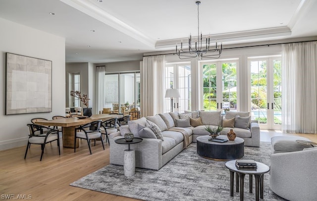 living room with a notable chandelier, plenty of natural light, a raised ceiling, and light hardwood / wood-style flooring