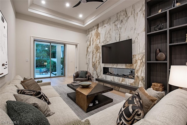 living room featuring light wood-type flooring, a tray ceiling, ceiling fan, and a fireplace