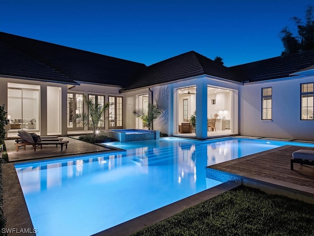 pool at twilight with a patio and an in ground hot tub