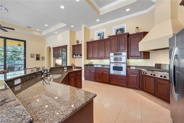 kitchen with stainless steel appliances, a tray ceiling, dark stone countertops, custom range hood, and sink