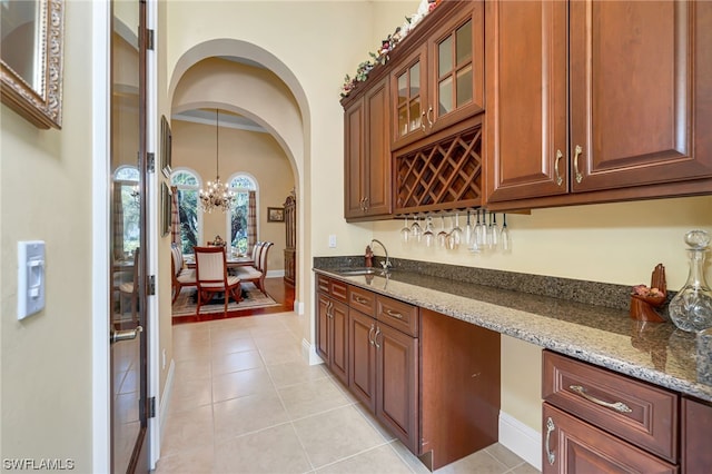 bar featuring dark stone countertops, sink, light tile patterned flooring, hanging light fixtures, and a chandelier