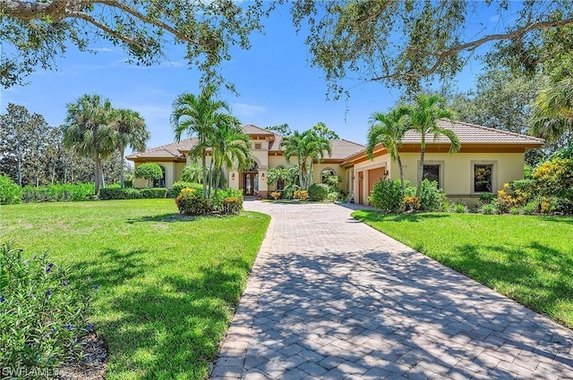 mediterranean / spanish house featuring decorative driveway, a garage, a front lawn, and stucco siding